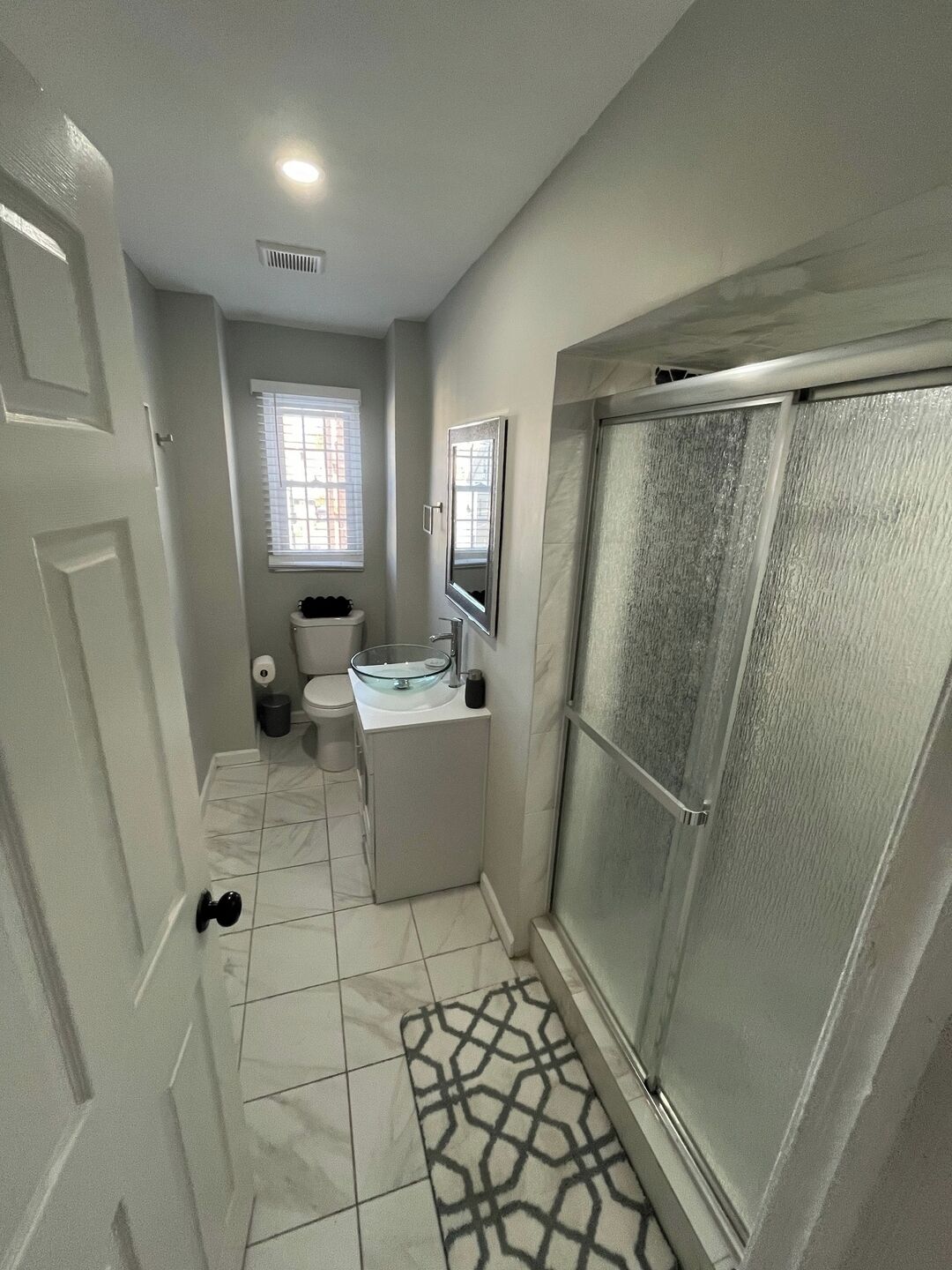 Ein Badezimmer mit Glasdusche, Toilette, Waschbecken mit Spiegel und Fenster mit Jalousien.