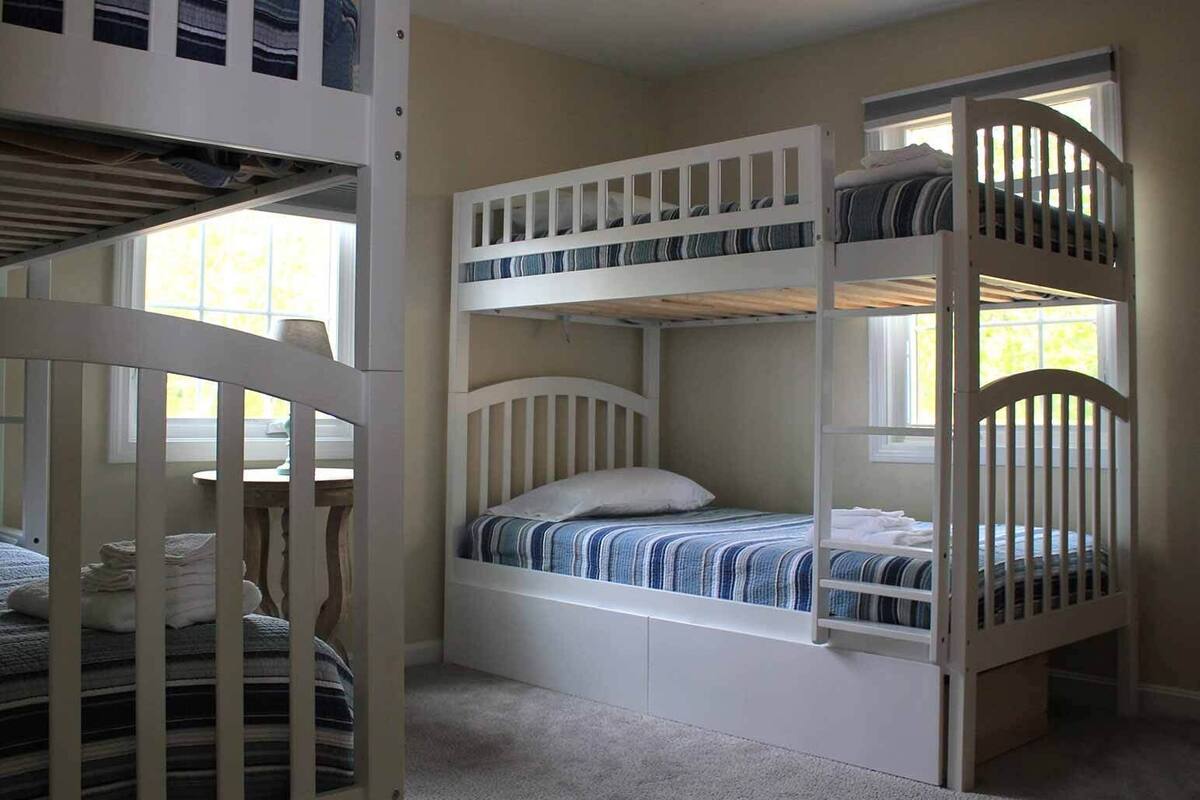 A bunk bed room with a desk and chair, a window, and a door.