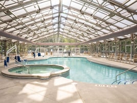 Piscina interna com teto de vidro, cadeiras de descanso e hidromassagem.