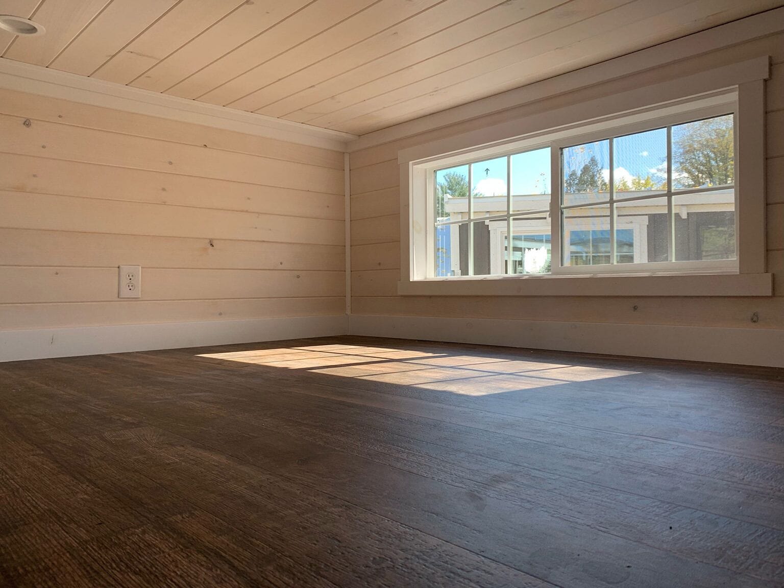 A room with wooden walls, a large window, and a dark wooden floor.