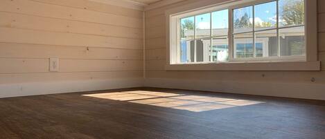 A room with wooden walls, a large window, and a dark wooden floor.