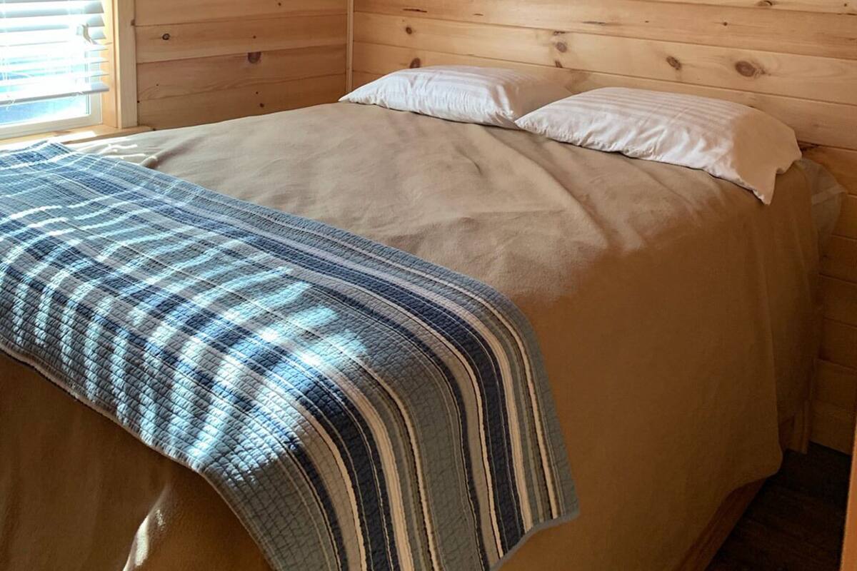 A wooden room with a bed, a window with blinds, and an air conditioning unit.