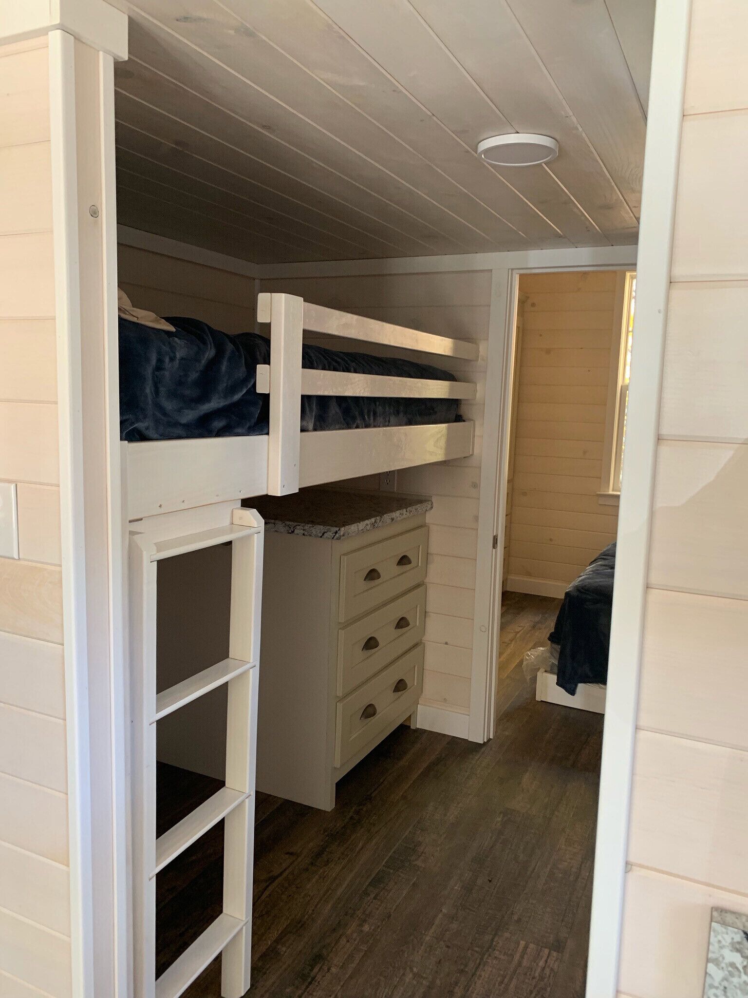 Habitación compacta con literas, un pequeño tocador con cajones y una lámpara en el techo.