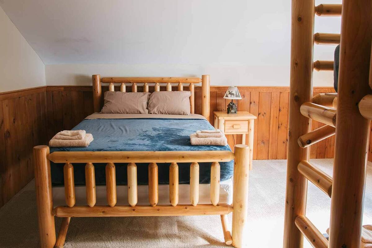 A wooden bed with a headboard, a nightstand with a lamp, and a wooden ladder.