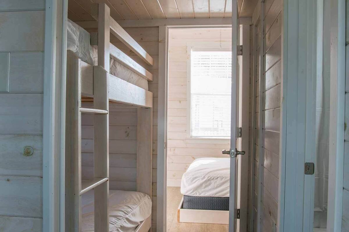 A wooden room with a bunk bed, a window with blinds, and a door.