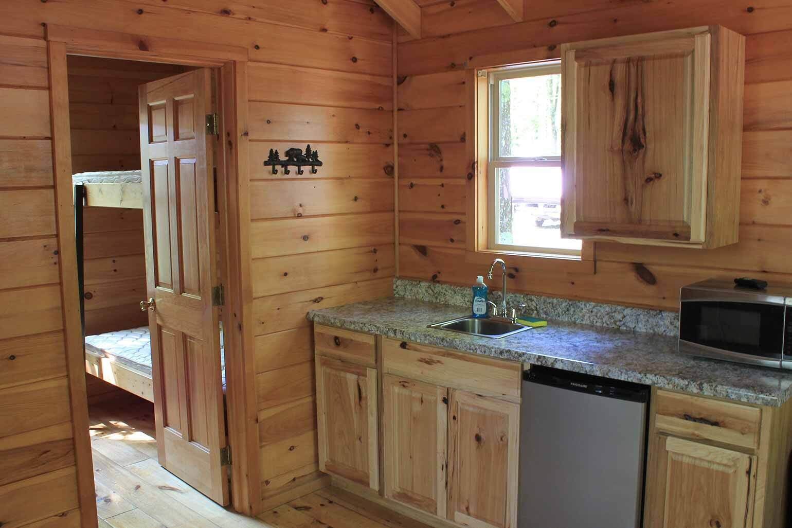 A wooden cabin interior with a kitchen area, including a sink, a microwave, and a dishwashing unit.