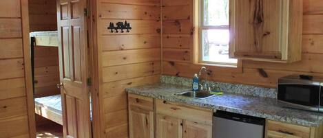 A wooden cabin interior with a kitchen area, including a sink, a microwave, and a dishwashing unit.