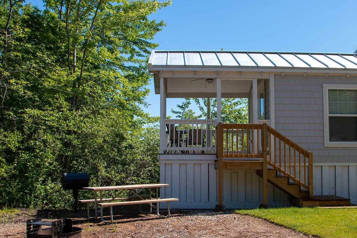 A small cabin with a porch, a wooden staircase, and a picnic table.