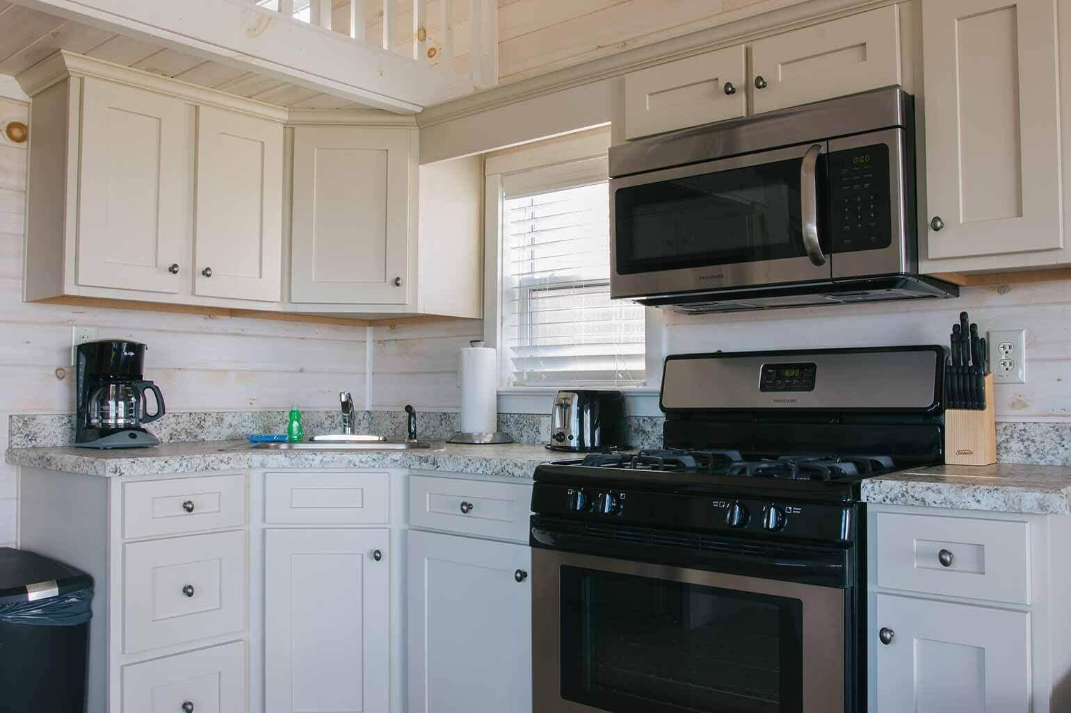 A kitchen with white cabinets, a stainless steel stove, a microwave, and a coffee maker.
