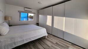 A bedroom with a bed, a window, an air conditioning unit, and a wardrobe. - Modern 2BR/2BA condo, upper floor, ocean breeze, short walk to Playa Chiquita (Sosúa)