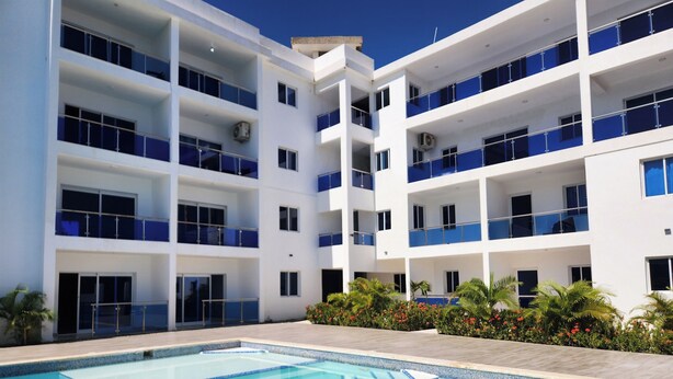 A modern hotel with a pool area, multiple balconies, and a clear blue sky. - Modern 2BR/2BA condo, upper floor, ocean breeze, short walk to Playa Chiquita (Sosúa)