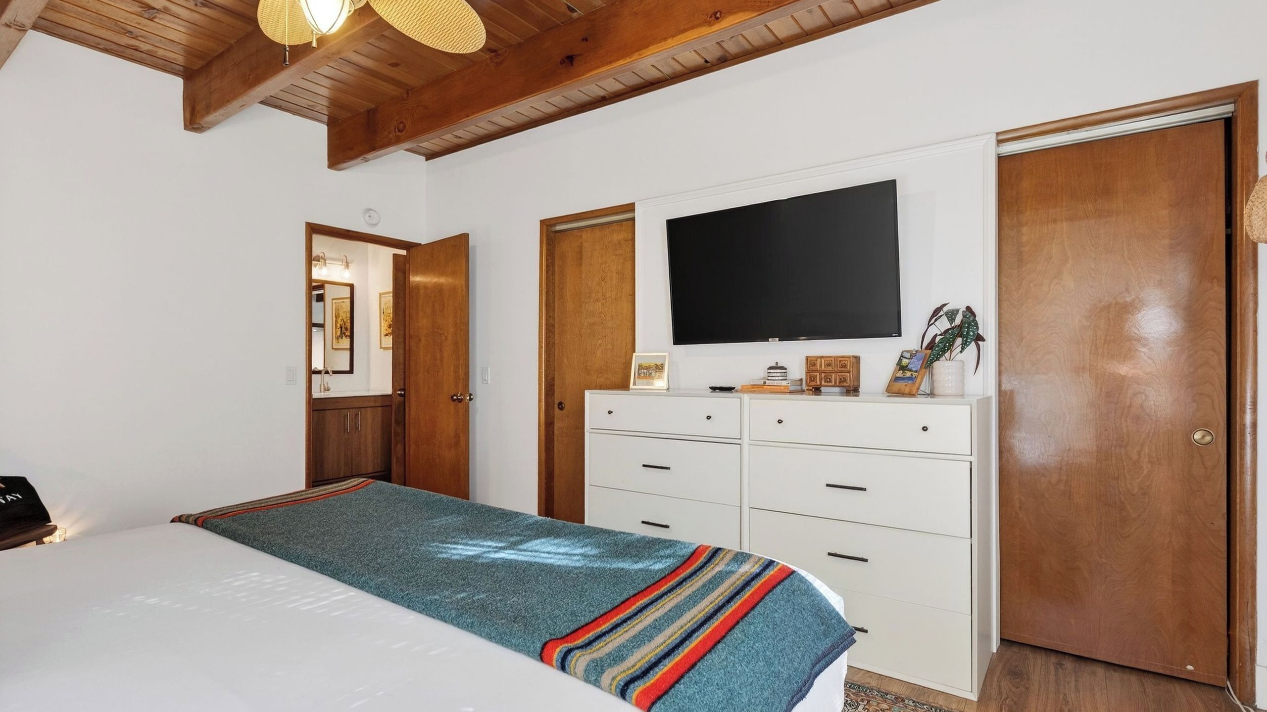 Een slaapkamer met een bed, een dressoir, een televisie en een deur.