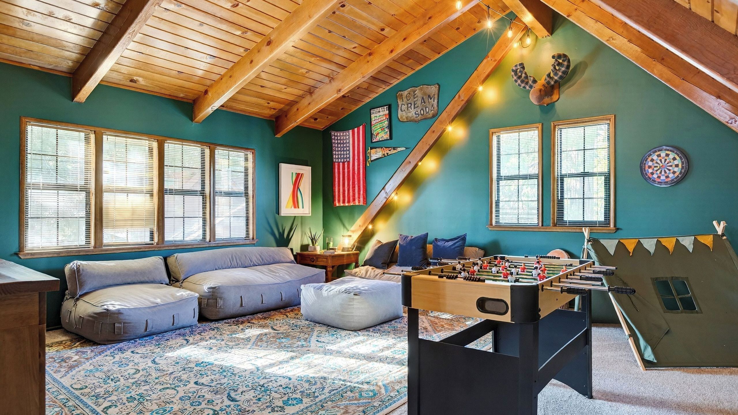 A cozy room with a wooden ceiling, a foosball table, a sofa, and a dartboard.