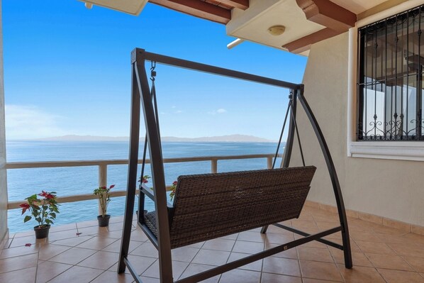 Ein Balkon mit einer Schaukel, Blumentöpfen und Blick auf das Meer.