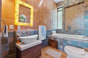 Ein Badezimmer mit einem großen Waschbecken, einer Badewanne und einer Toilette. Über dem Waschbecken hängt ein Spiegel und es gibt einen Duschbereich mit einer Mosaikwand.