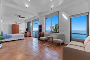 Ein geräumiges Wohnzimmer mit Bett, Sitzecke und großen Fenstern mit Meerblick.