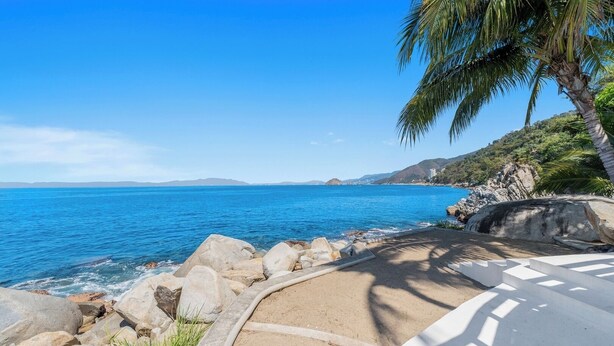 A coastal view with a clear sky, rocky shoreline, and a palm tree. - With sea views / View Next to the Oxxo viewpoint (Mismaloya Aguacate)