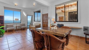 A spacious living area with a large wooden dining table, comfortable seating, and large windows offering ocean views. - With sea views / View Next to the Oxxo viewpoint (Mismaloya Aguacate)