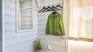 Um corredor com paredes azul-claras, uma jaqueta verde pendurada em um cabide preto, um vaso com planta e uma porta branca com janela.