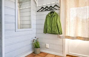 Ein Flur mit hellblauen Wänden, einer grünen Jacke, die an einem schwarzen Kleiderbügel hängt, einer Topfpflanze und einer weißen Tür mit Fenster.