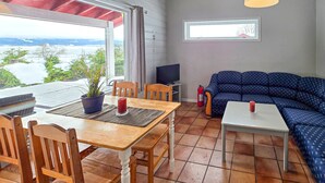Uma sala de estar acolhedora com uma mesa de madeira, cadeiras, um sofá azul, uma televisão e vista para o exterior.