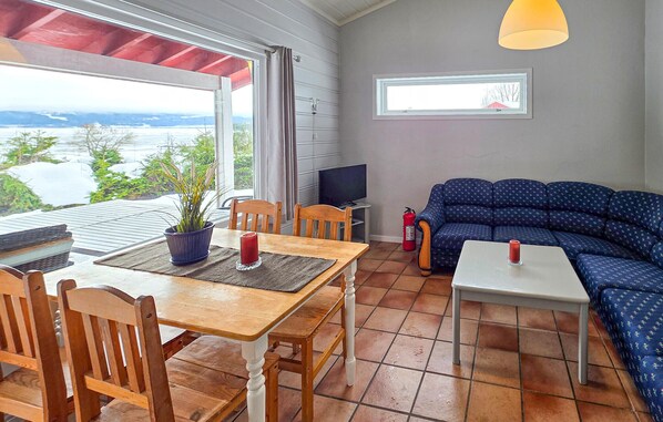 A cozy living room with a wooden table, chairs, a blue sofa, a television, and a view of the outdoors.