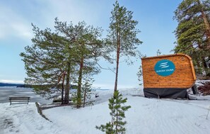 A wooden sign with the text "AURORA SAUNA" in a blue circle, surrounded by snow and trees.