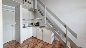 Eine kompakte Küche mit weißen Schränken, einer Mikrowelle, einer Kaffeemaschine und einem Geschirrspüler. Außerdem ist eine weiße Tür und eine Treppe mit weißer Geländer zu sehen.