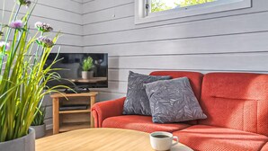 Ein Zimmer mit einem roten Sofa, einem Fernseher auf einem Holzboden, einer Kaffeetasse auf einem Tisch und einem Fenster mit Blick auf Bäume.