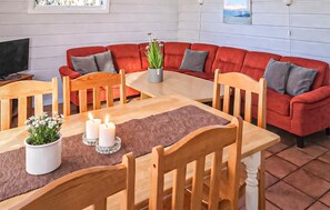 En hyggelig stue med en rød sofa, træstole, et spisebord med stearinlys og en potteplante.