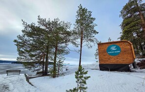 Ein Holzschild mit der Aufschrift 'Aurora Sauna', umgeben von Schnee und Bäumen.