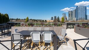 Une terrasse extérieure avec une table et des chaises, la silhouette de la ville en arrière-plan et une vue sur un parc.