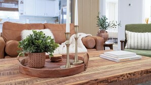 Ein Wohnzimmer mit einem braunen Sofa, einem Couchtisch mit Tablett, einer Zimmerpflanze und einem Buch mit dem Titel 'House Rules' von Myoujelyn Smith.