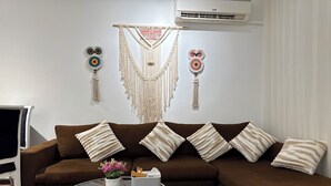 A living room with a brown sofa, a glass coffee table, and a macrame wall hanging. - Brand New Boho Apartment Sharm (South Sinai Governorate)