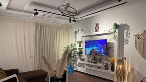 A modern living room with a round glass coffee table, a brown sofa, a TV mounted on a white wall, and decorative plants. - Brand New Boho Apartment Sharm (South Sinai Governorate)