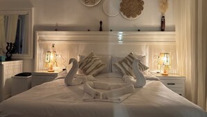 A neatly made bed with decorative swan pillows, bedside lamps, and wall decor including a mirror and circular plates. - Brand New Boho Apartment Sharm (South Sinai Governorate)