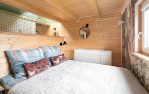 A cozy wooden cabin bedroom with a bed, pillows, a dresser, and a mirror on the wall.