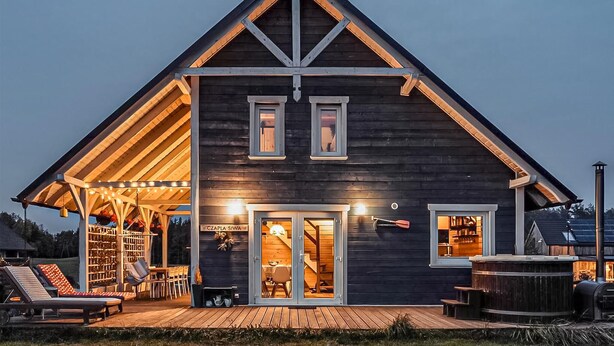 Een modern houten huis met een puntig dak, een overdekte veranda en een hottub.