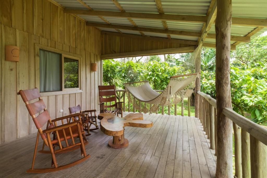 A wooden deck with rocking chairs and a hammock, overlooking lush greenery.