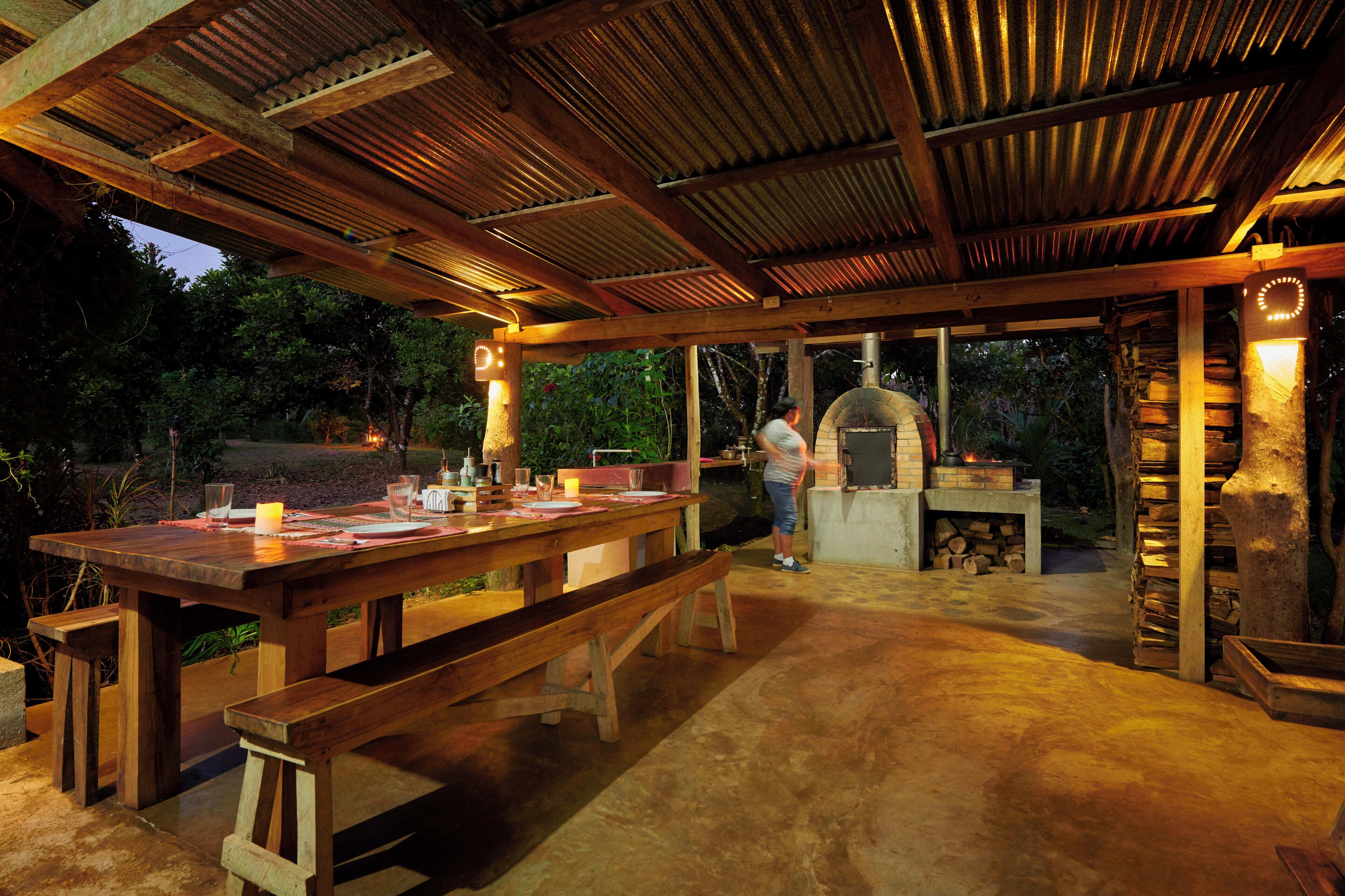 Une terrasse extérieure avec une table et des bancs en bois, un four en briques et une cheminée en pierre.