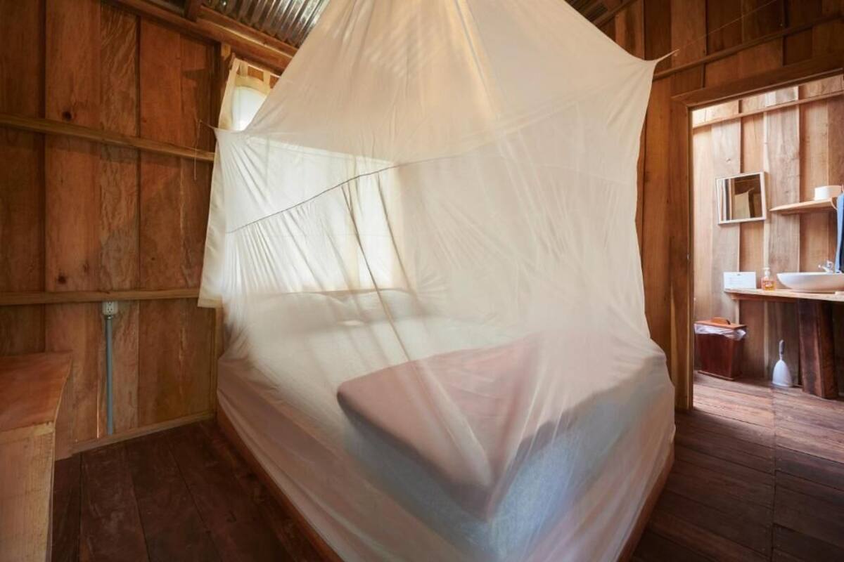 Een houten kamer met een bed, overdekt met een wit klamboes.