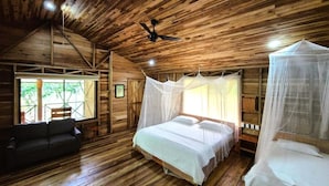 A wooden cabin bedroom with a bed, a sofa, and a ceiling fan. - Finca Amistad Cacao Lodge (Bijagua)