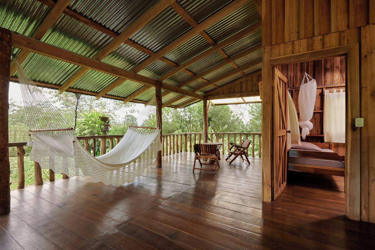 Een houten terras met een hangmat, stoelen en een bed.