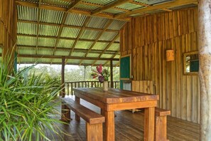 A wooden deck with a table and benches, surrounded by a corrugated metal roof. - Finca Amistad Cacao Lodge (Bijagua)