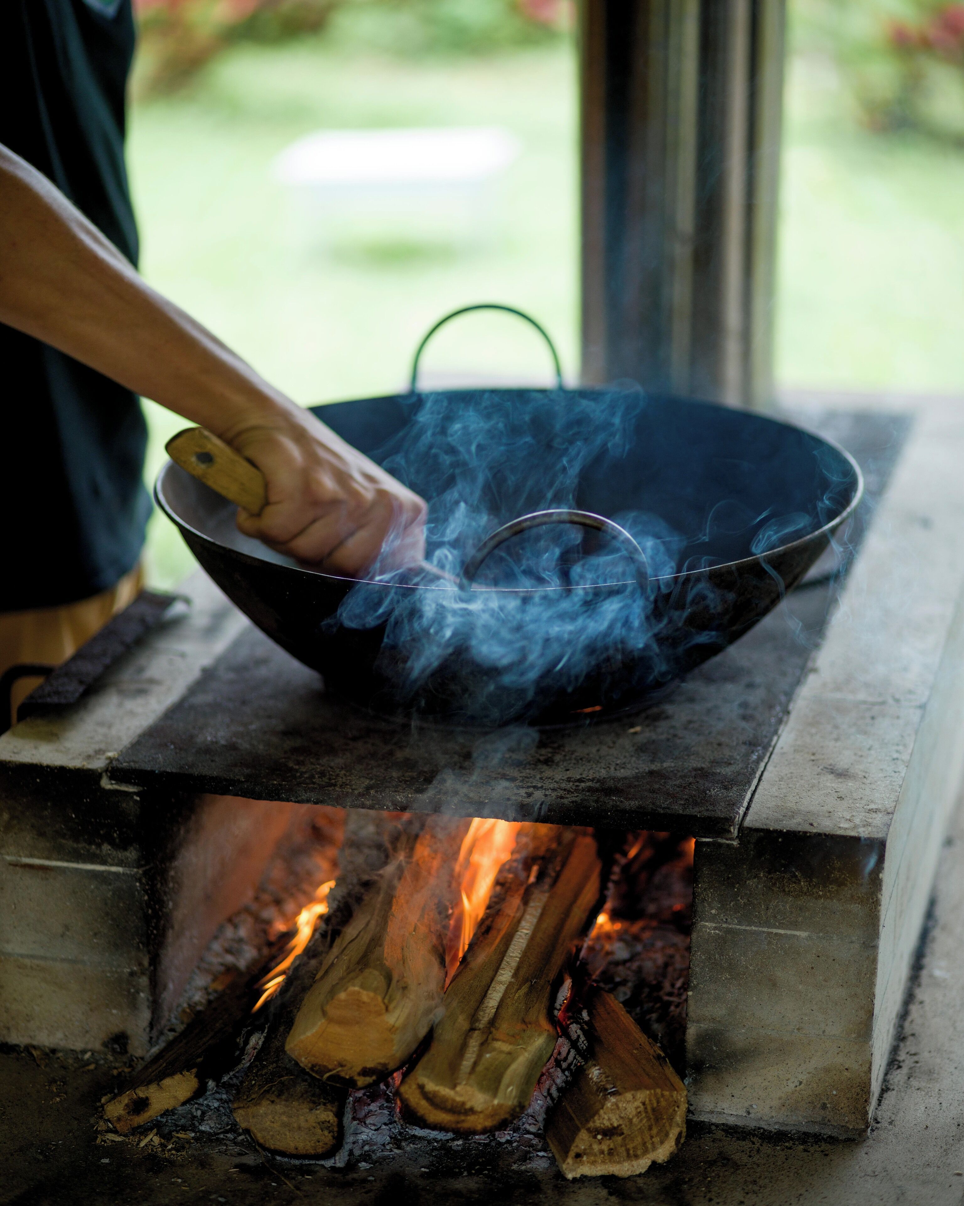 Una persona cocinando con un wok sobre fuego abierto.