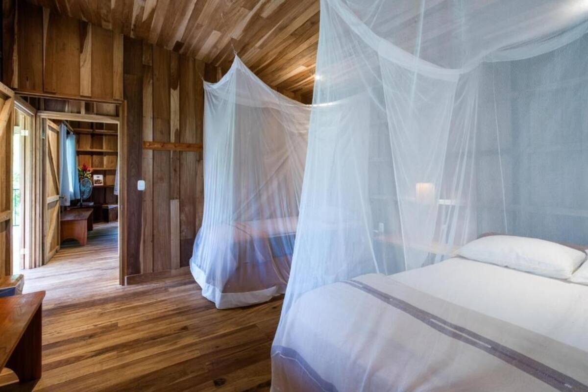 Een kamer met houten vloer, een bed met witte beddengoed en een hemelbed met een wit net.