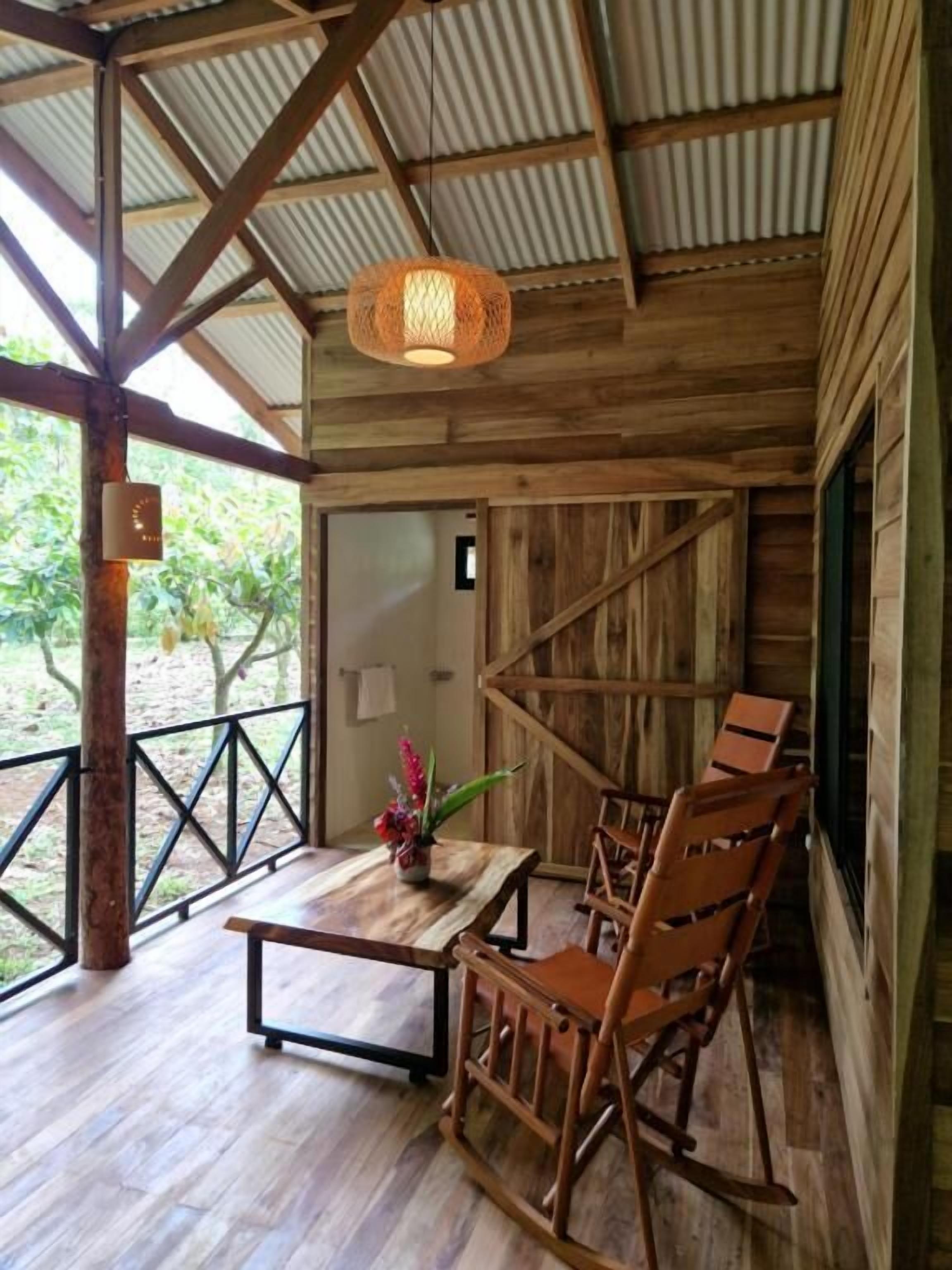 A rustic wooden interior with a dining area, including a table and chairs, a hanging light fixture, and a view of the outdoors.