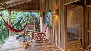 A wooden deck with a hammock, rocking chairs, and a round table. - Finca Amistad Cacao Lodge (Bijagua)