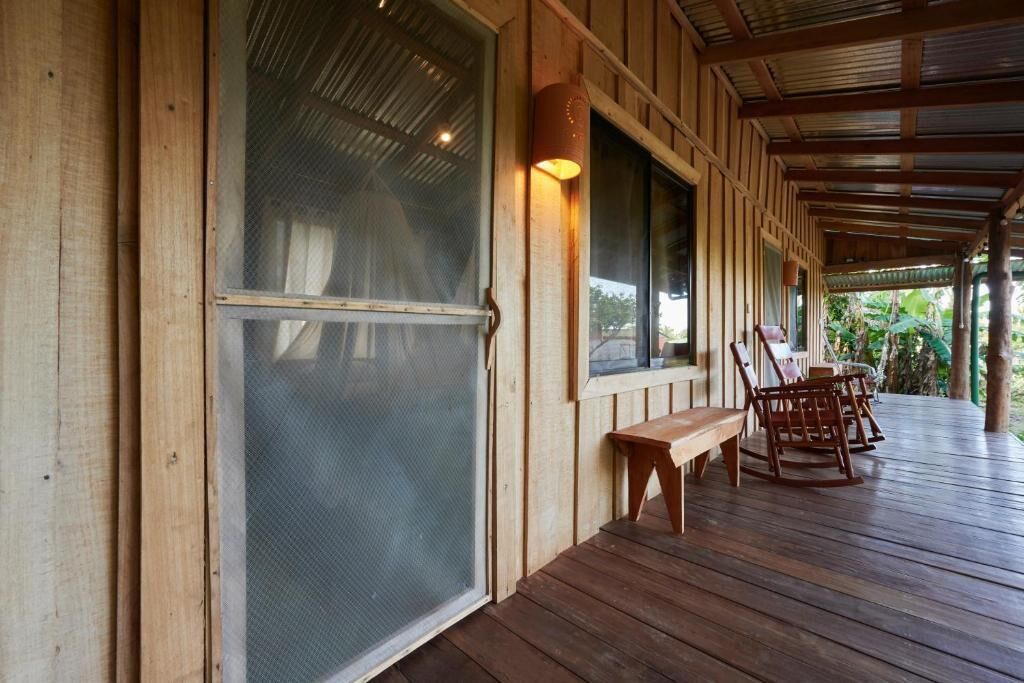 A wooden deck with a bench and chairs, a covered area with a roof, and a large window with a screen.