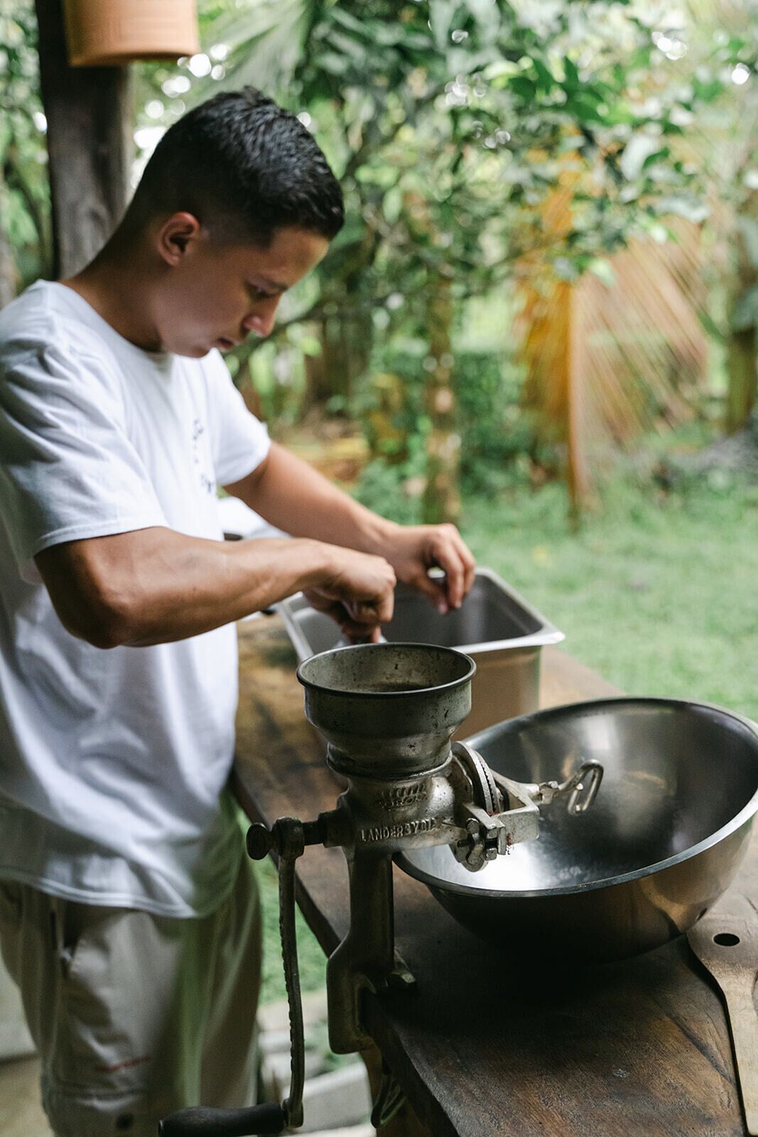 A person using a manual coffee grinder outdoors.